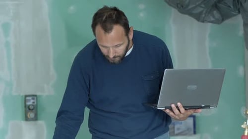 Man Working with Laptop and Blueprints Indoors
