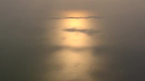 setting sun reflects on the sea with some shadow patches casted by the clouds filmed from high abov