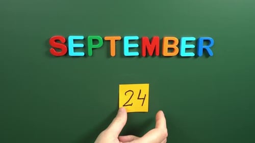 Hand sticking a sticker 24 September calendar day on school board. 24 date of September. Twenty