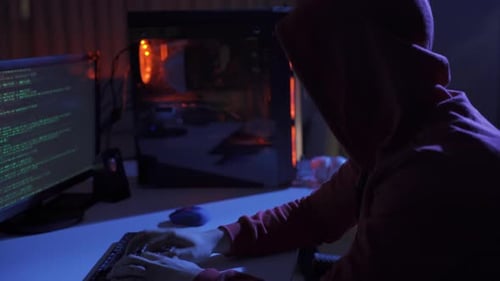 Side view of hacker sitting near computer monitors with green code screens.