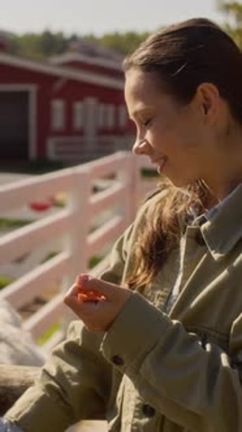 Vertical of Happy Female Caretaker Feeding Cow with Carrots on Country Farm