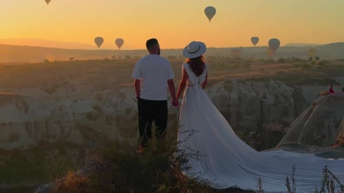 Young couple stands on mountain and watches balloons fly in sky