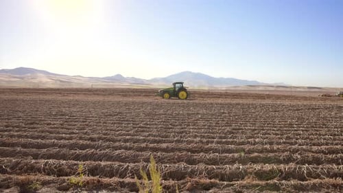 Side View of Distant Modern Tractor Working in the Field Hills on Backgound
