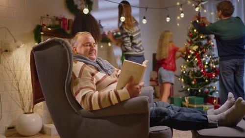 Family Decorating Christmas Tree as Grandfather Reads