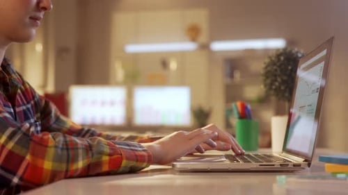 Side View of a Young Woman Typing on the Keyboard of a Laptop