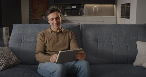 Man Smiles Using Tablet on Couch