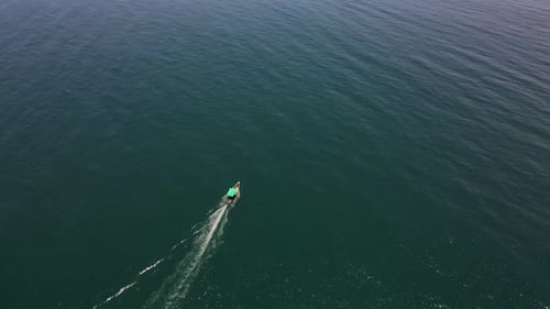 Top-down aerial drone shot of a fishing boat in the center of the calm, deep blue ocean waters.