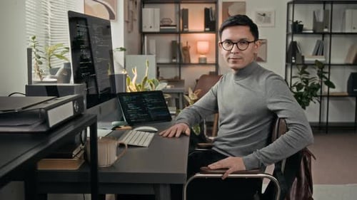 Portrait of Positive Young Software Engineer Sitting at Work Table in IT Office