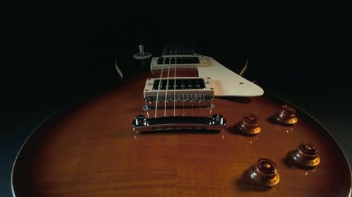 Slow tracking up the body of a Gibson Les Paul electric guitar, covering the volume and tone control