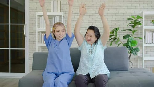 Female physiotherapist raising hands of active senior woman in hospital