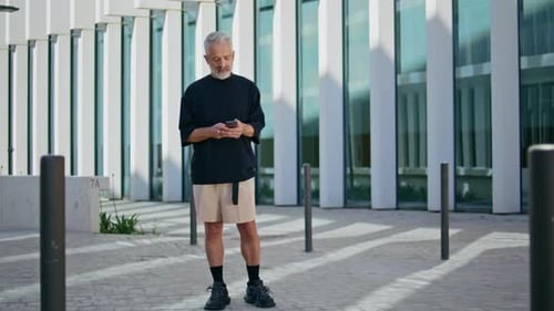 Senior Man Uses Phone Outside Modern Building