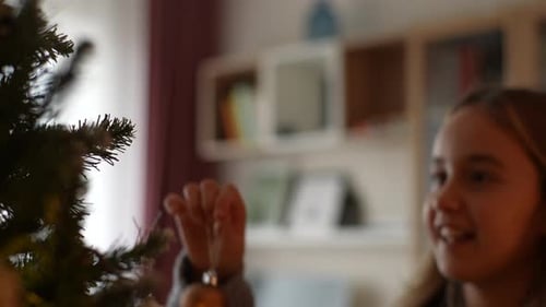 Girl Decorates Christmas Tree with Ornament at Home