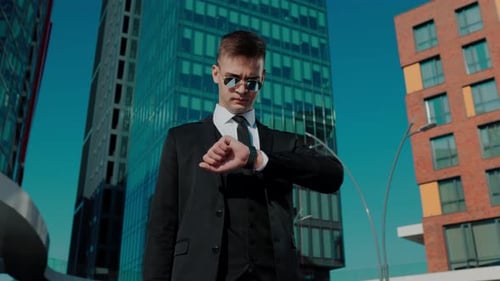 Confident Young Executive Checks Time in City Center