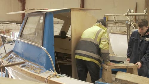 Carpinteiros maduros e jovens trabalhando juntos consertando barcos de fibra de vidro
