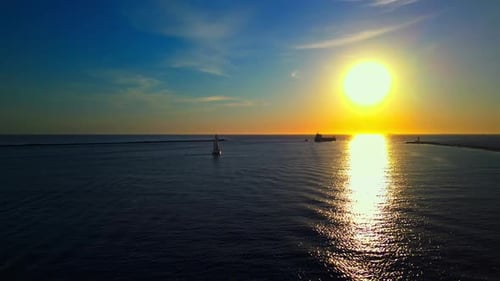 An Aerial View Captures a Serene Sunset Over a Calm Ocean with Sailboats and a Ship Sailing