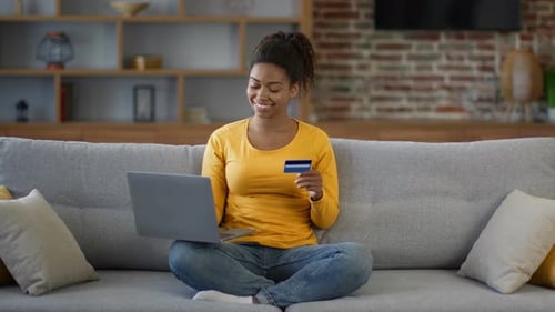 Young Positive African American Woman Doing Financial Payment Via Laptop with Credit Card at Home