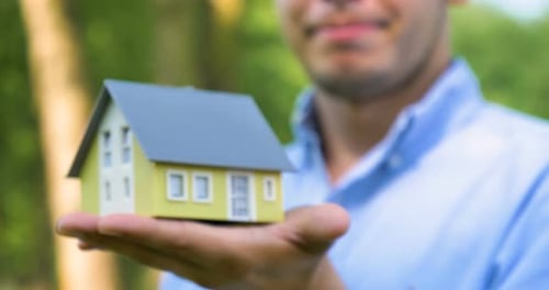 Man Holds Miniature House Model in His Hand