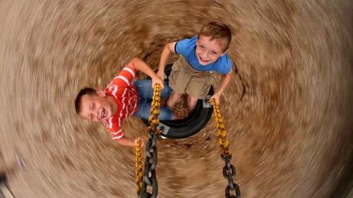 Two Young Boys Spinning Tire Swing At School Playground