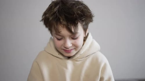 Handsome teenage kid sitting in front of camera. Kid puts some tangerines as his eyes. Close up.