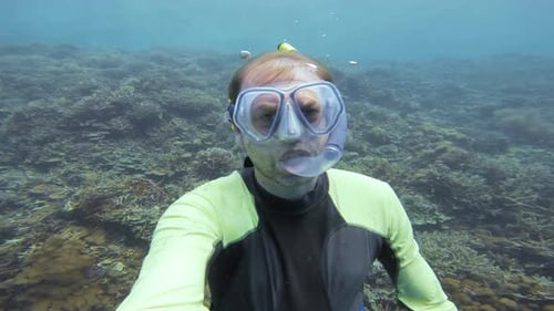 Un plongeur apnéiste remonte lentement vers la surface, avec le récif corallien en arrière-plan.