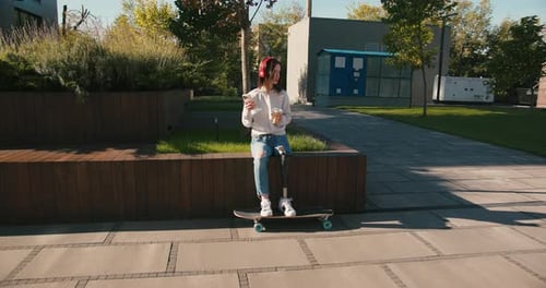 Female with Prosthetic Leg Sitting on Longboard Woman with Prosthetic Leg Wearing Red Headphones and