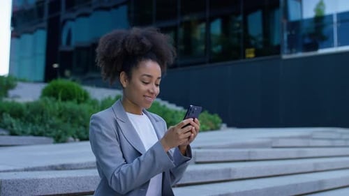 Woman Using Phone on Steps Outside Modern Building