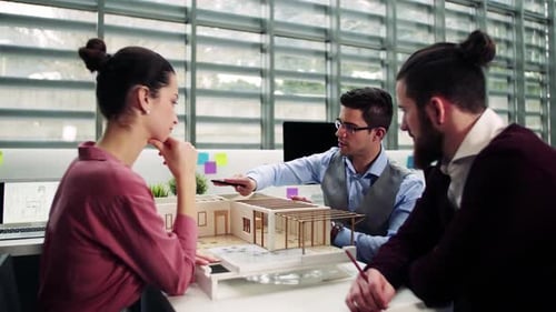 Group Of Young Architects With Model Of A House In Office, Talking.