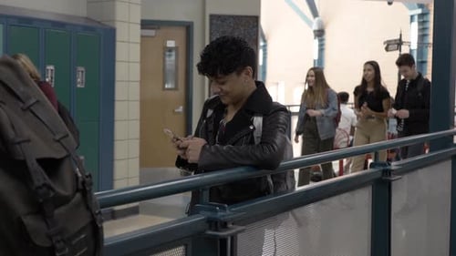 Asian high school student smiling and texting on smart phone in school corridor