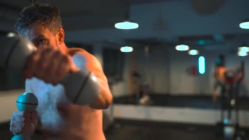 Boxer Practices Punches with Dumbbells in His Hands in the Gym in the Evening