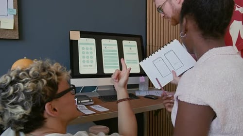 Diverse Team Discussing Mobile App UI Displayed on Computer at Office