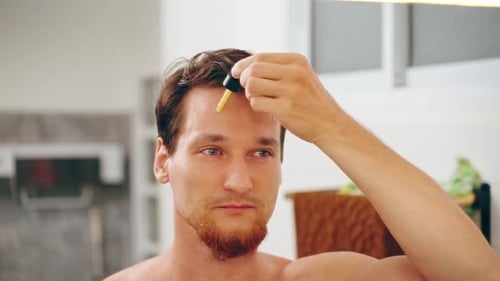 Man Applies Yellow Serum to Forehead in Bathroom