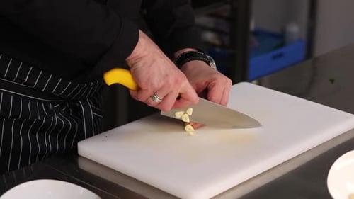 Chef Dicing Garlic With Knife on Cutting Board