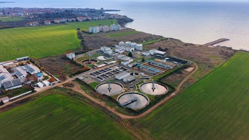 Wastewater treatment plant area in the green fields at the seashore. City scenery at backdrop.