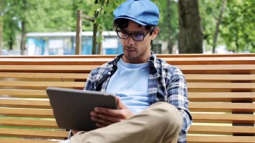 Creative man browsing online with tablet pc on city street bench near fixed gear bike