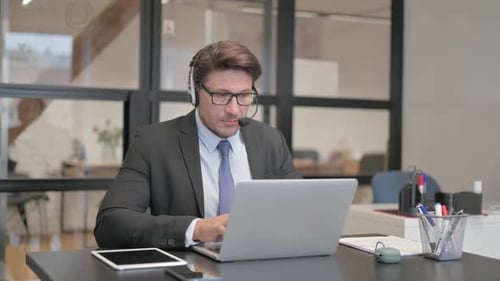 Call Center Man Looking at Camera while Working on Laptop with Headset