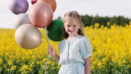 Charming Girl Standing at Yellow Field with Air Balloons
