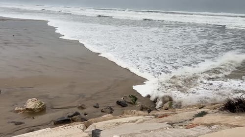 Turbulent storm waves coming in on a sandy beach with grey threatening sky above
