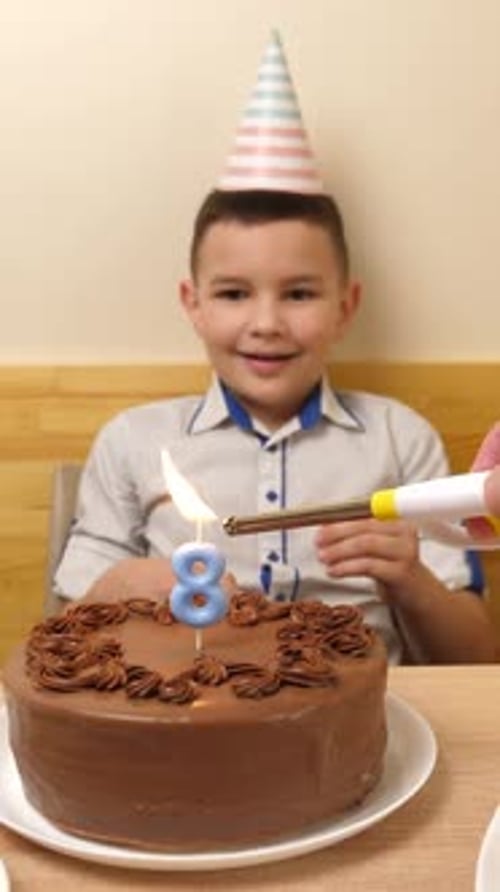 07. The boy is sitting in front of a table with a festive cake, in which a candle in the form of the