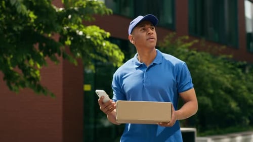 Puzzled African American Courier Man Delivery Guy Male Postman Looking at Mobile Phone Check Address
