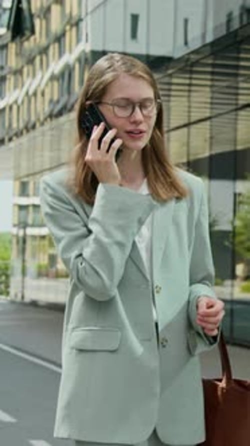Young Female Manager Speaking on Phone when Walking along City Street