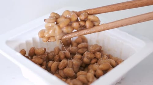 Wooden chopsticks holding Japanese natto beans on white background side view.