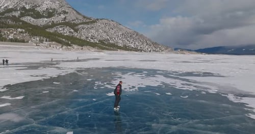 aerial view of man ice skating on frozen abraham lake in laberta, canada