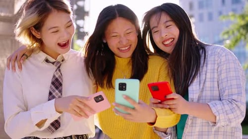 Three Friends Laughing at Smartphones in Urban Setting