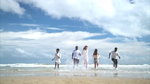Gruppe verschiedener Freunde, die Spaß am Strand haben, spazieren gehen und an einem sonnigen Tag in die Wellen springen