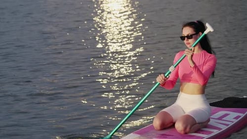 Woman Paddleboarding on Water at Sunset