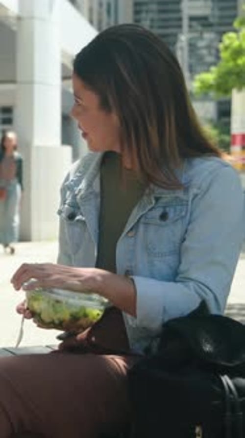 Vertical video: Spotting passerby, woman removing lid and eating at bench with salad bowl, fork