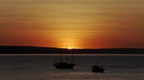 Dramatic Sunset over Calm Ocean with Silhouetted Boats