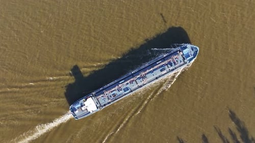 Tanker sails gracefully across river as the hull slices through water. Aerial