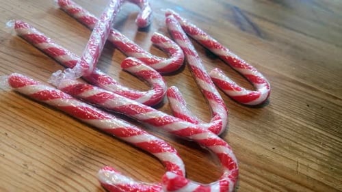 Glänzende, in Plastik verpackte gestreifte Weihnachts-Zuckerstangen auf hölzernem Küchentisch, Heimdekoration, rotierend