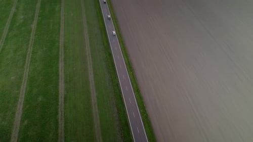 Drohnenaufnahme aus der Luft, die Autos verfolgt, die durch Straßen zwischen landwirtschaftlichen Feldern und grüner Landschaft fahren